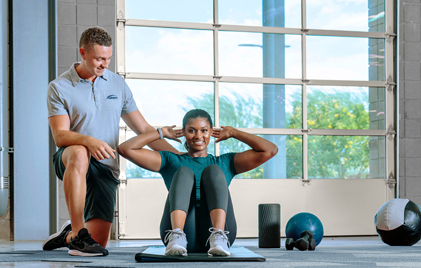 Female doing sit up with male personal trainer supporting