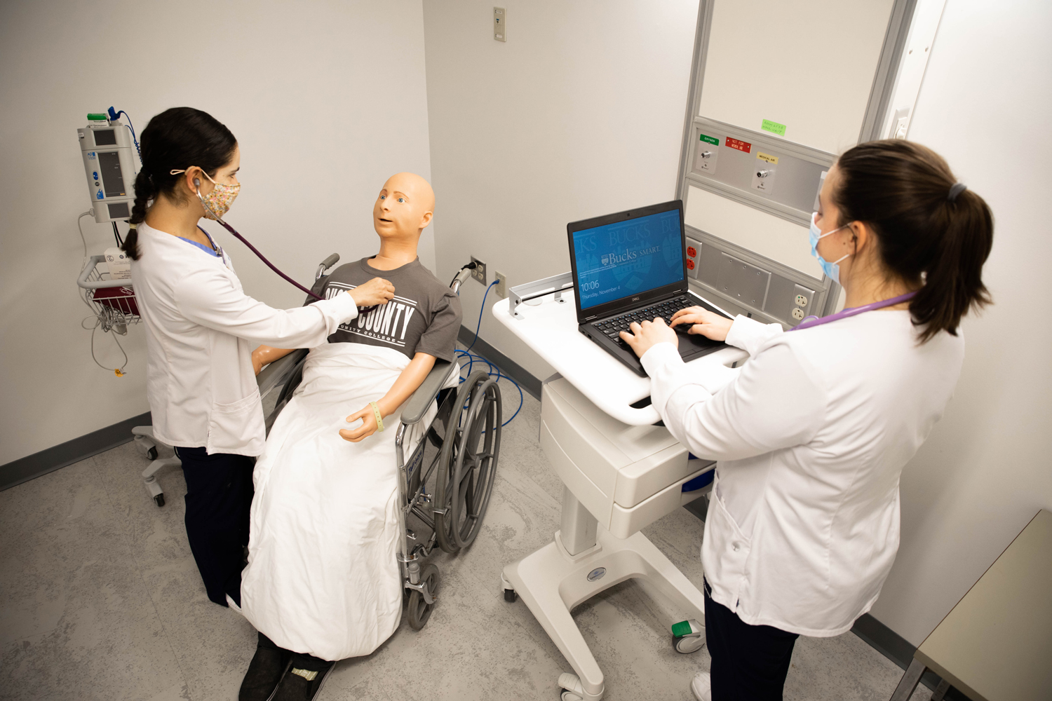 Nursing students conduct a patient assessment on a medical mannequin in a simulation lab.