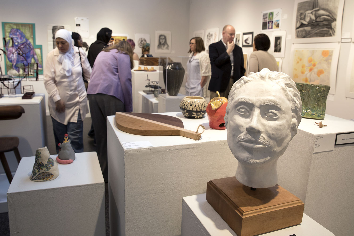 Art exhibition with various sculptures and paintings on display, with visitors observing.