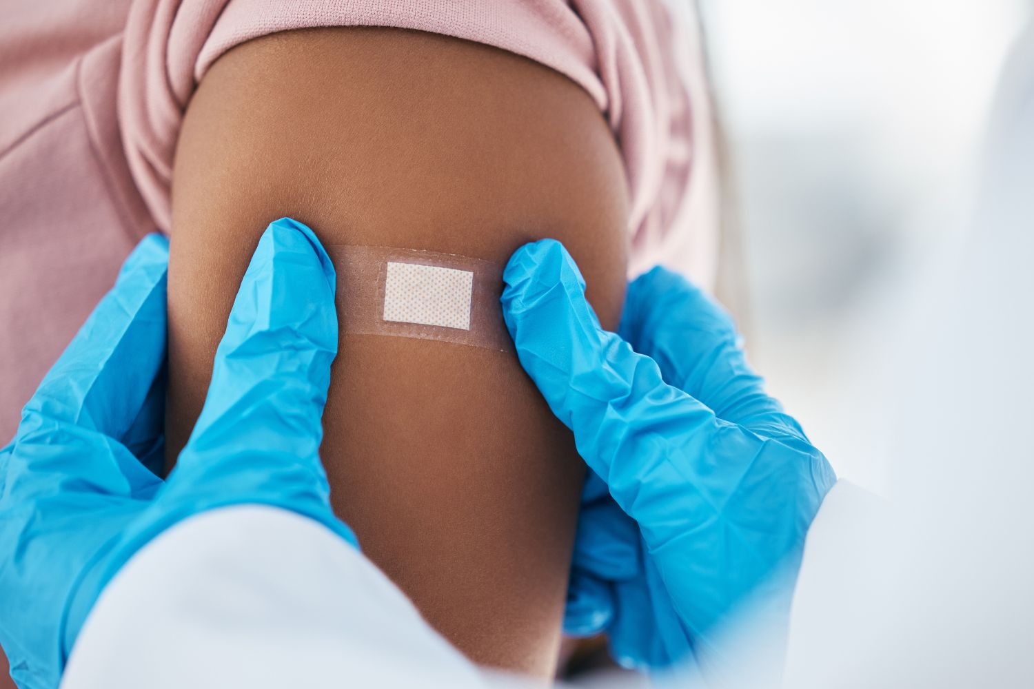 Close-up of gloved healthcare workers holding an upper arm with a small adhesive bandage.